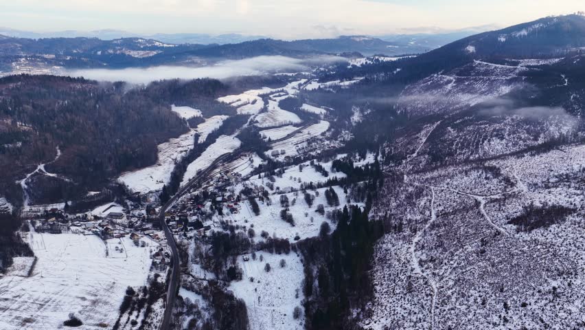 Aerial view of a snowy valley with villages, winding road and forested hills near Terchová, Slovakia. Winter rural landscape, mountains, nature and peaceful countryside atmosphere.