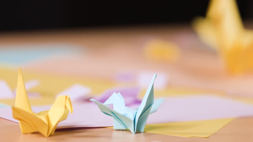 Static close-up shot of yellow and blue paper cranes resting on a wooden crafting table