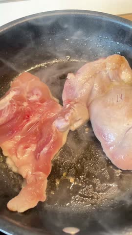 Two pieces of chicken are cooking in a pan. The pan is black and the chicken is pink