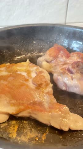 Two pieces of meat are cooking in a pan. The meat is brown and has a crispy texture