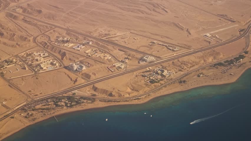 Sunlit aerial view from an airplane window over the desert near Aqaba, Jordan, showcasing the deep blue Red Sea, dramatic landscapes, and the coastline