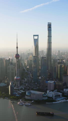 Vertical drone shot circling the sunlit Pudong skyline of Shanghai, hazy morning