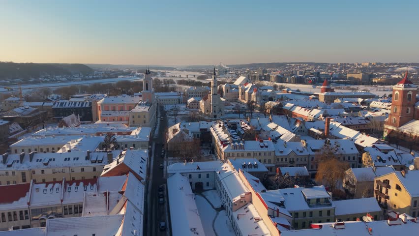 Drone video capturing a stunning aerial view of snow-covered Kaunas Townhall in Lithuania's Old Town. The winter scene is complemented by historic architecture under soft morning light.