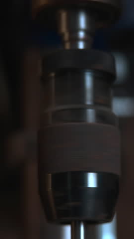 Close up of a spinning drill bit lowering from a drill press in a workshop. Media