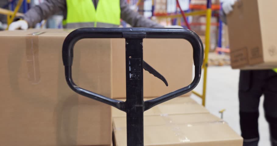 Warehouse workers moving boxes with pallet truck. Warehouse team moves a pallet through aisles for delivery, shipping, and order fulfillment. Strong concept of efficient teamwork logistics.