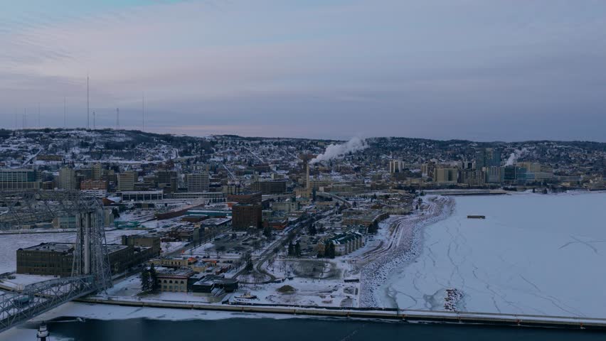 Wide aerial view of Duluth city and the frozen shoreline of Lake Superior during winter dusk.