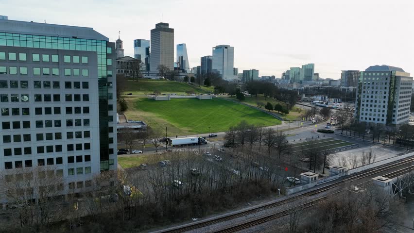 Aerial flyover shot of busy road in Nashville, green grass on hills and famous skyline skyscrapers of downtown in distance. Peaceful sunrise in the morning. Wide shot.