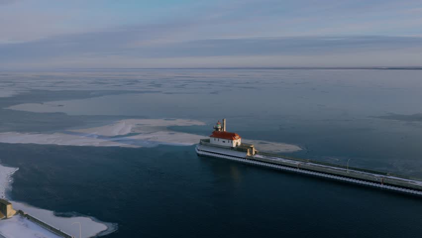 Aerial view of the Duluth North Pier Lighthouse at the end of a pier, surrounded by pancake ice sheets on the deep blue waters of Lake Superior.