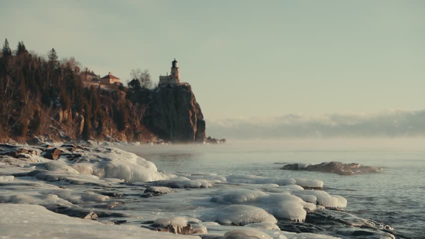 Close-up of frozen ice formations on the shore of Lake Superior with Split Rock Lighthouse and sea smoke in the distance.