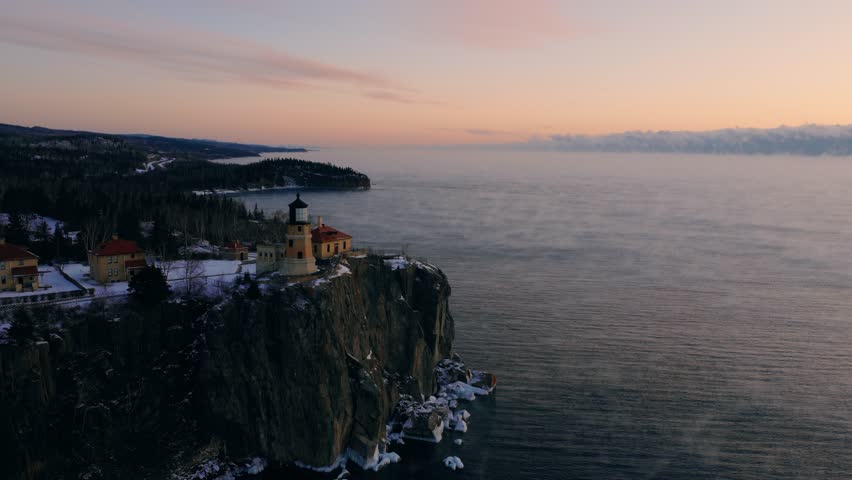 Cinematic aerial rotation of Split Rock Lighthouse, capturing golden sunrise light on the historic buildings and rugged cliffs.