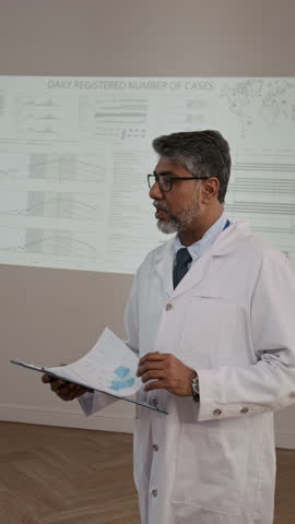 Vertical view of mature male virologist in classic lab coat delivering presentation on infection rate while taking part in medical seminar
