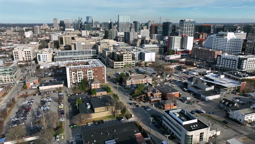 Daytime aerial view of downtown Nashville, Tennessee, showing dense urban skyline with modern office buildings, streets and neighborhoods under clear skies. Sunny day in winter. Wide shot.