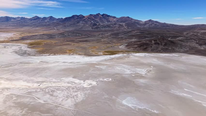Drone pans across salt flat with mountains and clear sky at high altitude.
