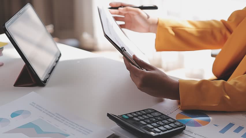 A person calculating financial data on a calculator with graphs and laptop nearby