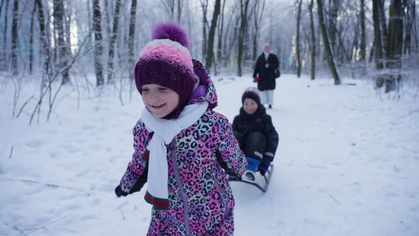 Children sledding in a snowy forest. Winter family games in nature, happy family moments.