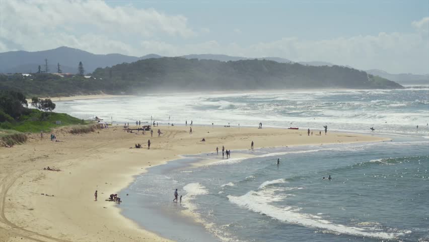Beach shoreline with people standing in shallow water and waves breaking, Sawtell, New South Wales, Australia.