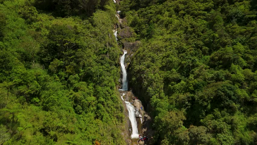 Drone flies over fast-moving mountain river rapids and white water at the base of the Cascadas Chamana waterfall surrounded by dense tropical rainforest in Banos de Agua Santa Ecuador