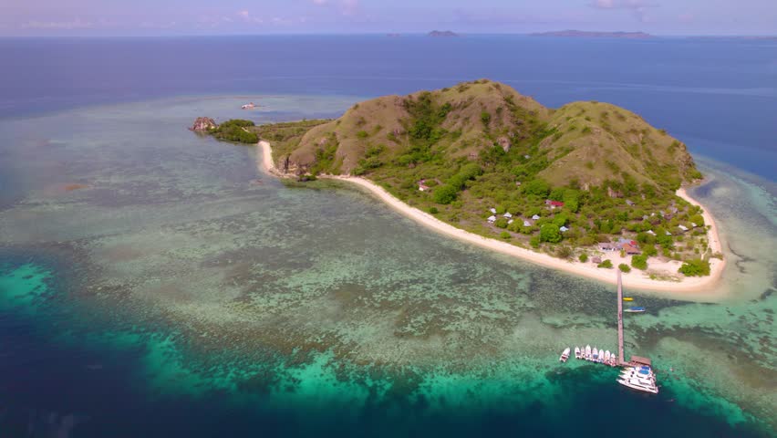 Orbital aerial revealing Kanawa Island, a small tropical island surrounded by crystal-clear turquoise waters and coral reefs in Komodo National Park, Indonesia.