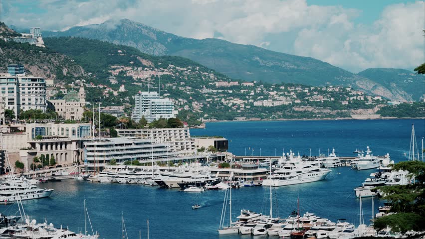 Stunning cinematic aerial view of monte carlo cityscape and port hercule with luxury yachts and boats, idyllic mountain landscape in background on sunny summer day, monaco