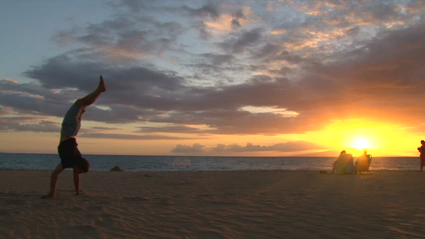 Model released man walks on his hands on sandy beach during sunset in Hawaii.
