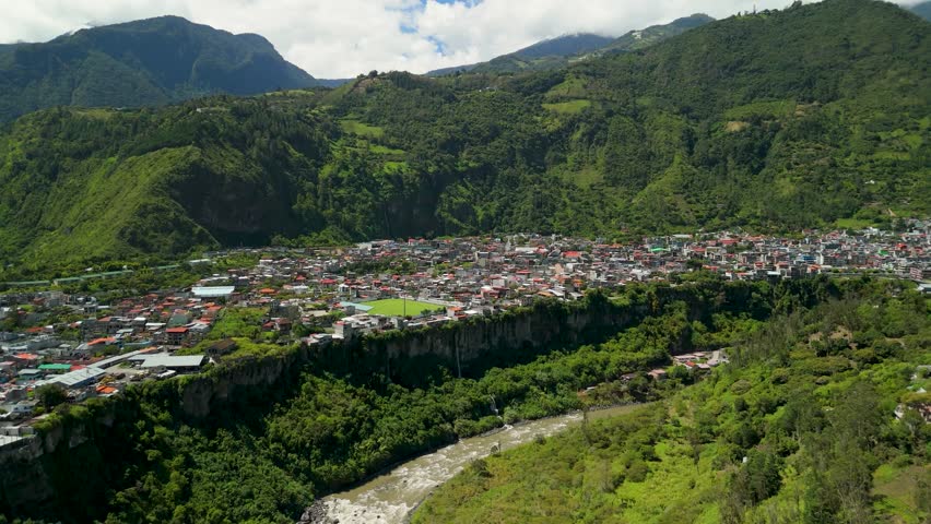 Drone flies over city of Banos de Agua Santa revealing urban landscape tucked between massive green mountains and steep cliffs in dramatic Andean valley of Tungurahua Ecuador