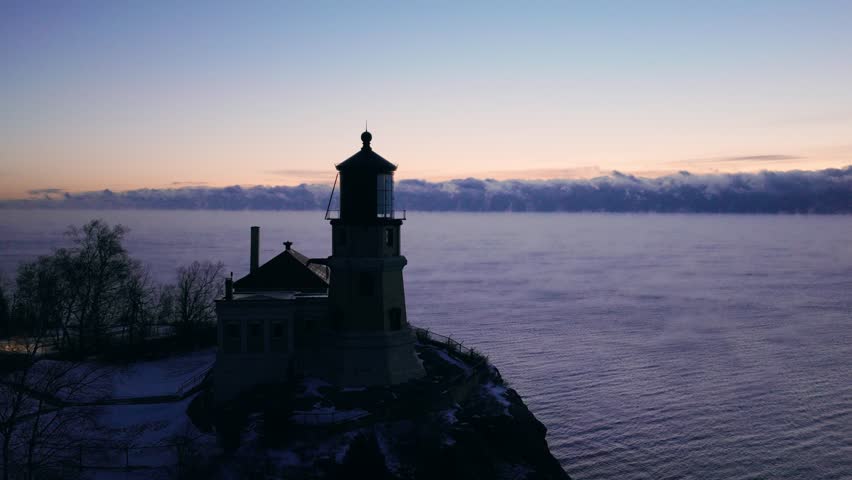 Split Rock Lighthouse silhouetted at twilight with the beacon rotating over a misty Lake Superior.