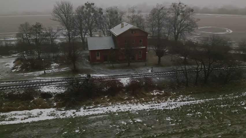 Aerial reveals old Rural brick railway station on single track line with passing loop in winter. Remote countryside scene suitable for travel, documentary, and vintagel use.