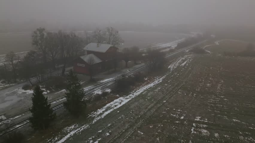 Aerial over old rural railway station on foggy winter morning. Atmospheric countryside transport scene suitable for documentary, travel, and historical visuals.