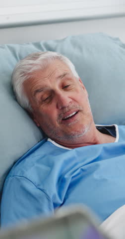 Hospital, talking and old man in bed with doctor for surgery feedback, online results and consulting. Healthcare, tablet and elderly person speaking for recovery, rehabilitation and medical service