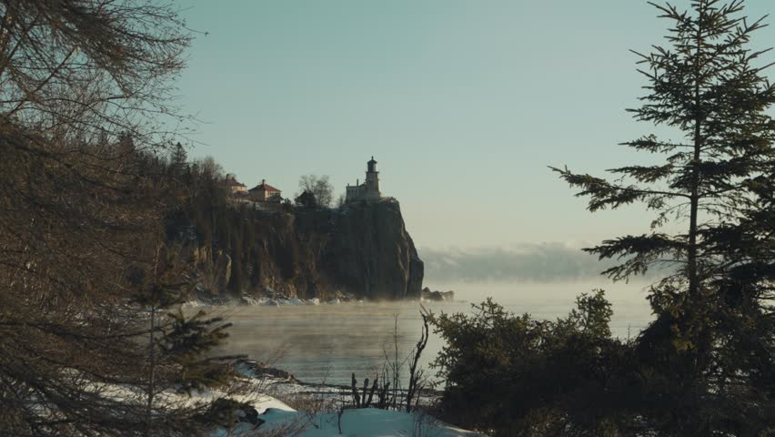 Cinematic wide shot of the historic Split Rock Lighthouse on a high cliff, with thick sea smoke rising from Lake Superior on a frigid Minnesota morning.