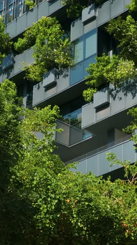 Modern eco-friendly glass office building with vertical garden and trees on balconies in urban environment in Bangkok city, Thailand. Green architecture, sustainable design, eco city