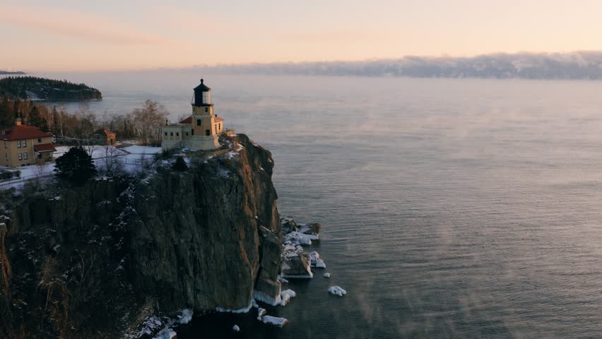 Aerial drone view of Split Rock Lighthouse on its iconic cliff over Lake Superior with winter sea smoke at dawn.