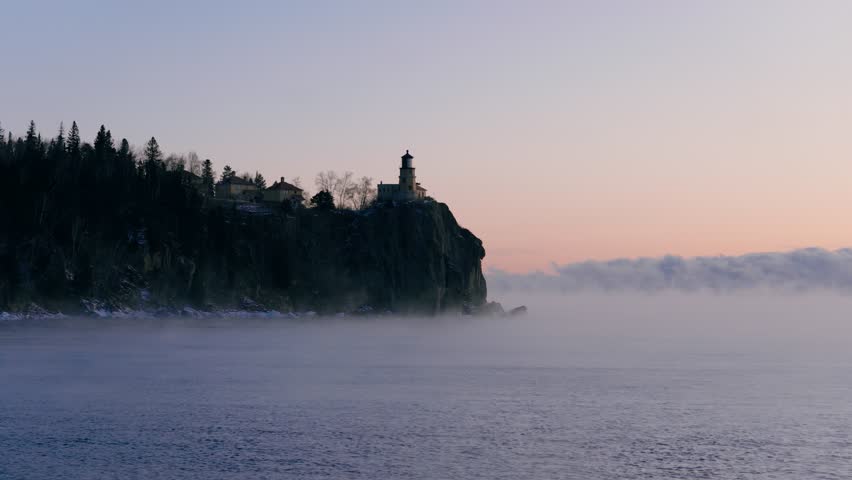 Split Rock Lighthouse emerges from heavy winter sea smoke and mist on a rugged cliffside during a subzero sunrise on Lake Superior.