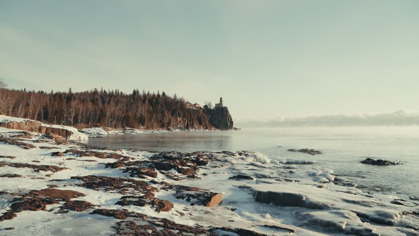 Wide view of the icy Lake Superior shoreline and Split Rock Lighthouse on a frozen winter morning with rising mist.