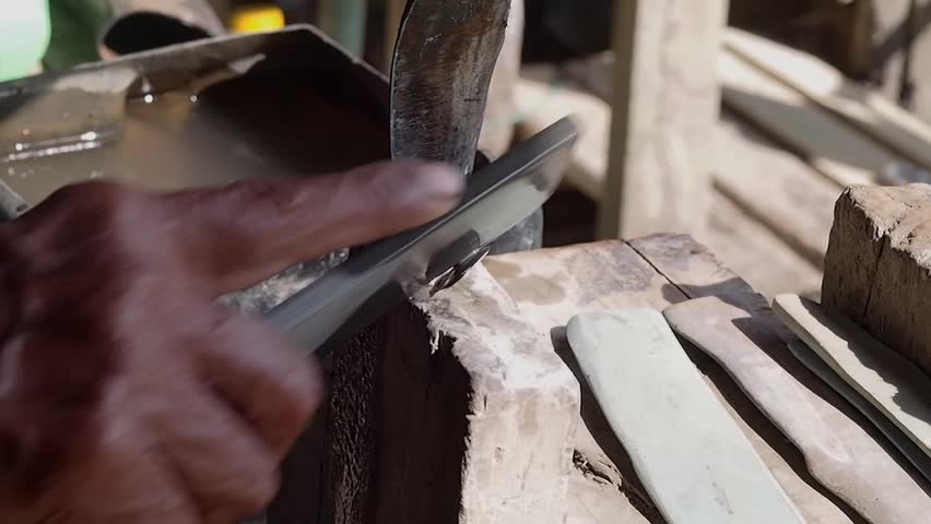 An old hand rubber worker sharpening tapping knife blade whetstone outdoors, manual tool care and precise motion close up rural rustic workshop