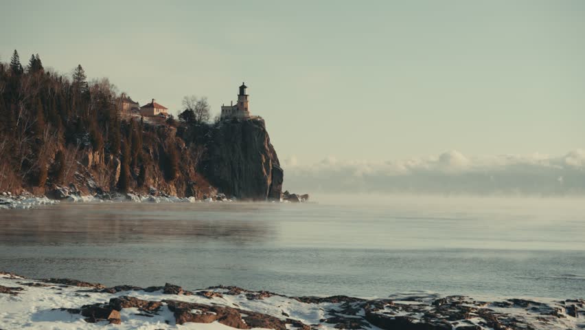 The historic Split Rock Lighthouse perched on a rocky cliff as winter mist drifts across Lake Superior at dawn.