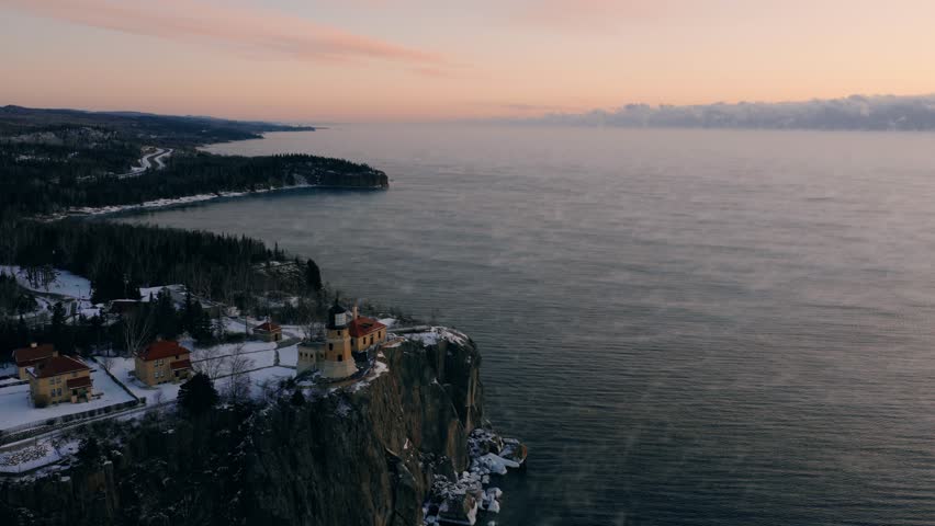 Wide aerial slide showing the proximity of Split Rock Lighthouse to the snowy North Shore forest and highway at sunrise.