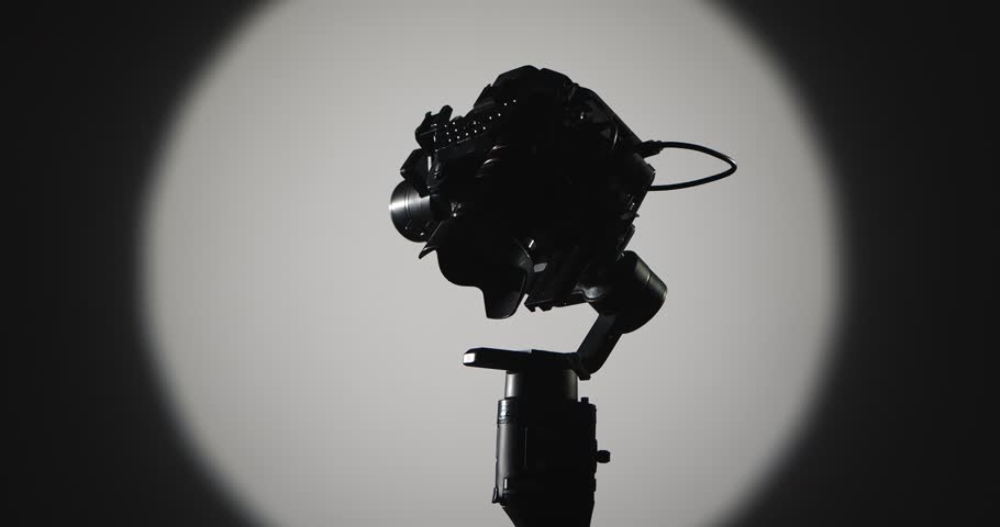 The operator stabilizes the camera mounted on a motorized stabilizer with a suspension, filmed against a bright round light on a dark background, symbolizing film production.