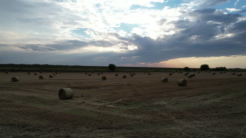 Drone flying above a vast field with hay bales at sunset