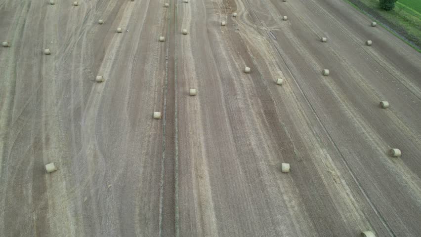 Aerial backwards flight over a harvested field with hay bales