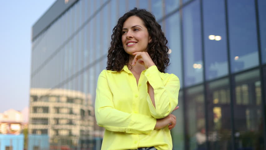 Portrait of a successful young professional woman with curly hair looking away and then smiling at the camera with her arms crossed