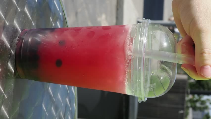 Girl is holding a plastic cup of refreshing orange bubble tea with tapioca pearls. Children drinking bubble tea on a summer walk. Drinks sold from a van. Happy children. refreshing summer fruity drink