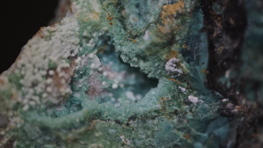 Macro image of gibbsite accompanied by chalcedony, goethite, and jarosite, sourced from the Copper Mountain district in Utah, United States, captured through a microscope objective at 2.4× magnification with a field of view of 15 mm. The gibbsite appears as white to pale gray granular and fibrous aggregates with vitreous to dull luster, formed during supergene alteration of aluminum-bearing minerals. Chalcedony occurs as bluish-green microcrystalline bands with fibrous texture, goethite as brownish-yellow coatings on grain boundaries, and jarosite as fine yellow-orange crystalline crusts. Surface is naturally developed by geological processes, showing no artificial modification. Lighting is even and directional, enhancing contrast between phases and revealing micro-topography without artificial enhancement. No digital filters or compositing were applied. This documentation serves as a source of scientific knowledge for the study of secondary mineral assemblages in oxidized copper deposits and the textural relationships among hydrous oxides, sulfates, and silicates. It supports educational materials in economic geology and mineral identification for visual analysis of habit, color, and association. Used in university-level courses for the study of weathering profiles, supergene enrichment, and non-destructive microstructural assessment. Such imagery aids in understanding the dynamics of the living world of Earth through surficial transformations that convert primary sulfides into economically relevant oxide and sulfate minerals. Through precise observation, this work reinforces empirical methods in earth science research and encourages deeper engagement with the structural and compositional diversity of planetary materials. The image reflects principles of documenting geological specimens without interference, supporting public education about mineral formation and the importance of conserving scientifically significant localities