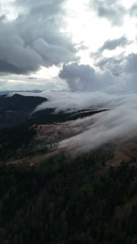 Breathtaking aerial view of a cloud waterfall rolling over green mountains and a small village, Black Sea region, Turkey.