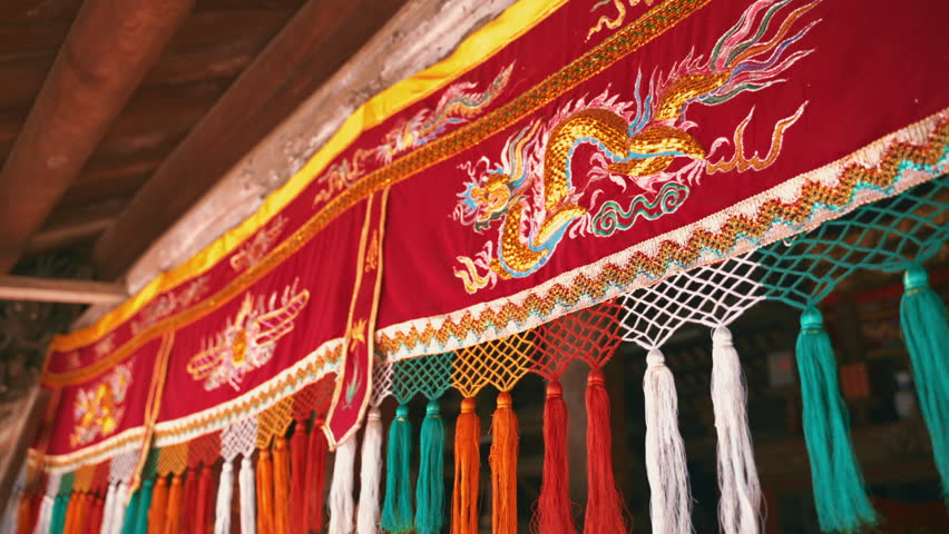 Close-up of a decorative red silk fabric featuring a golden dragon embroidery and vibrant multicolored tassels hanging in a traditional temple or ceremonial hall.