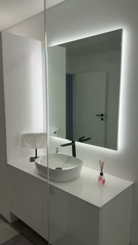 Vertical view of white bathroom vanity with sink faucet and backlit mirror