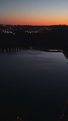 Aerial drone footage of calm lake at dusk with city lights glowing on horizon