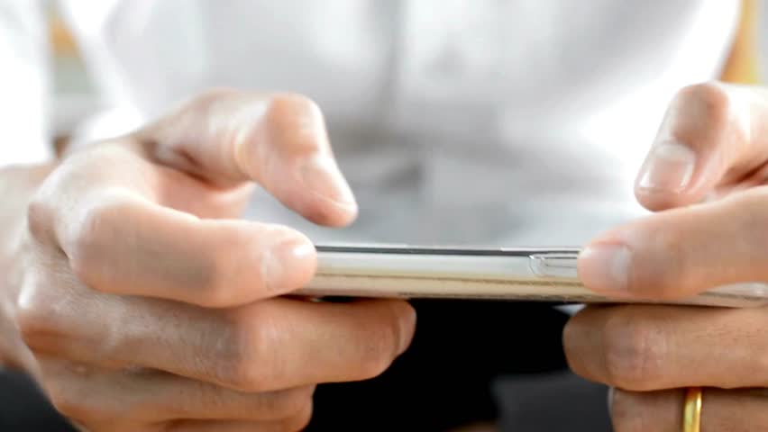 Close view of person playing game on smartphone or texting using cell phone. Hands quickly tapping and swiping across display. Person wears a white shirt.