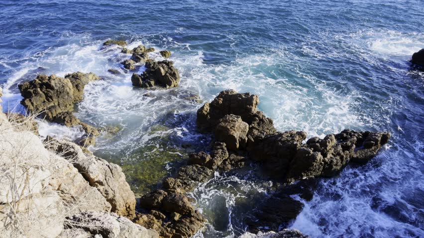 Waves crash against rugged rocks on a sunny day showing dynamic water motion