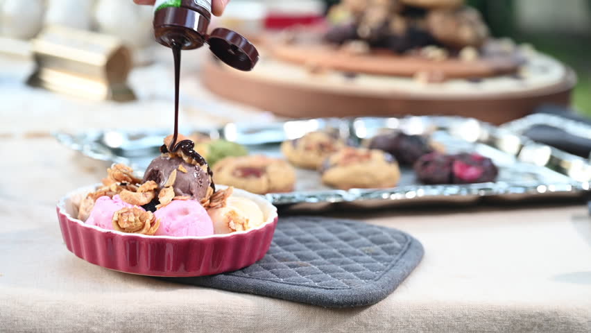Ice cream chocolate sauce hot fudge strawberry walnut dessert in ramekin with drizzle and scoop, cookie on tray, rich syrup pouring over pink scoops, nut crunch, outdoor table, natural light